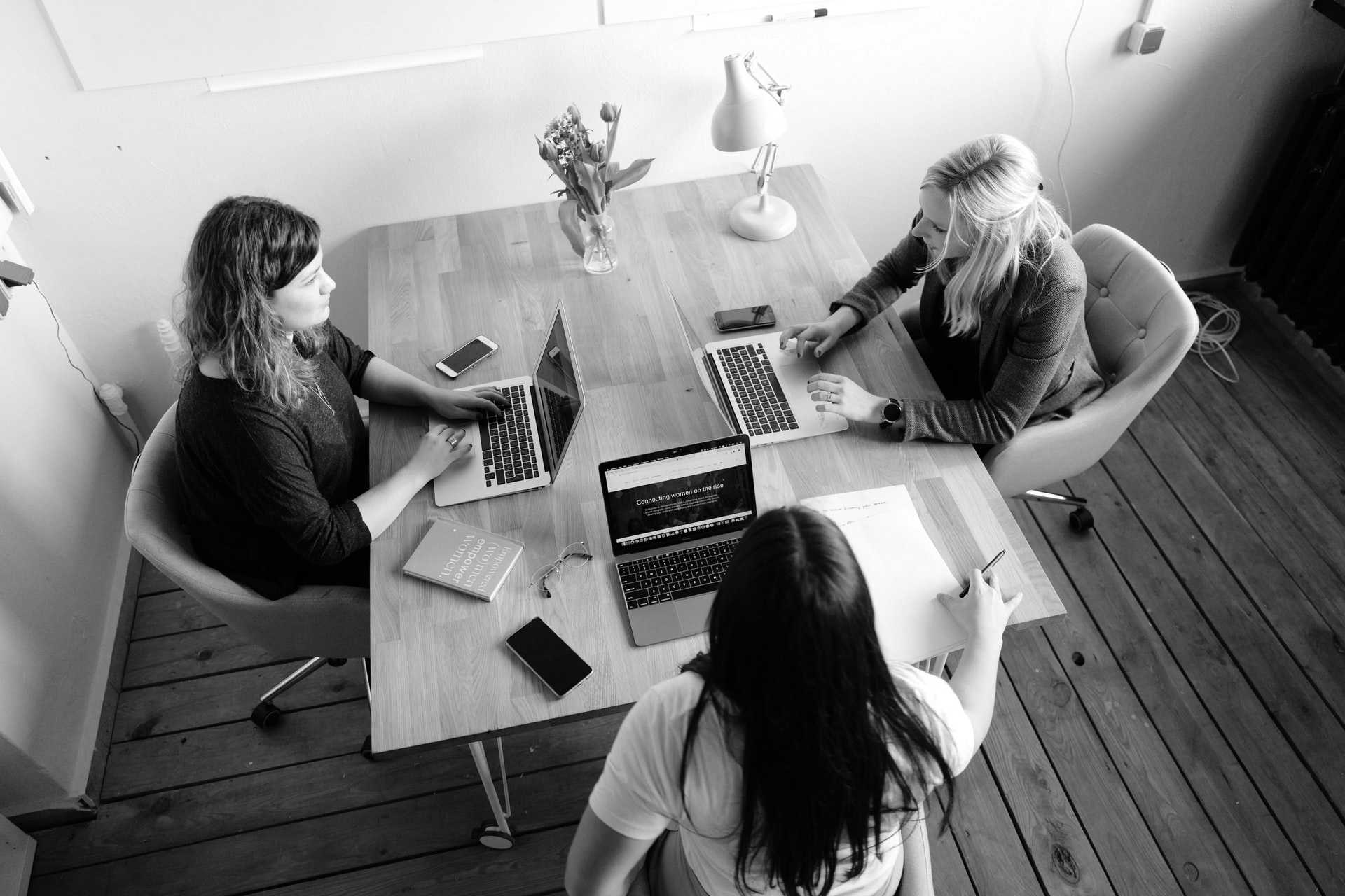 A table with three womens looking for their computer